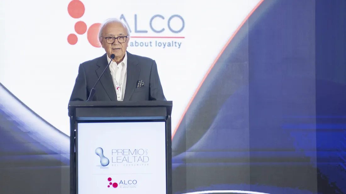 Orador en el atril de la ceremonia del Premio Lealtad, con el logotipo de Alco en la pantalla tras él